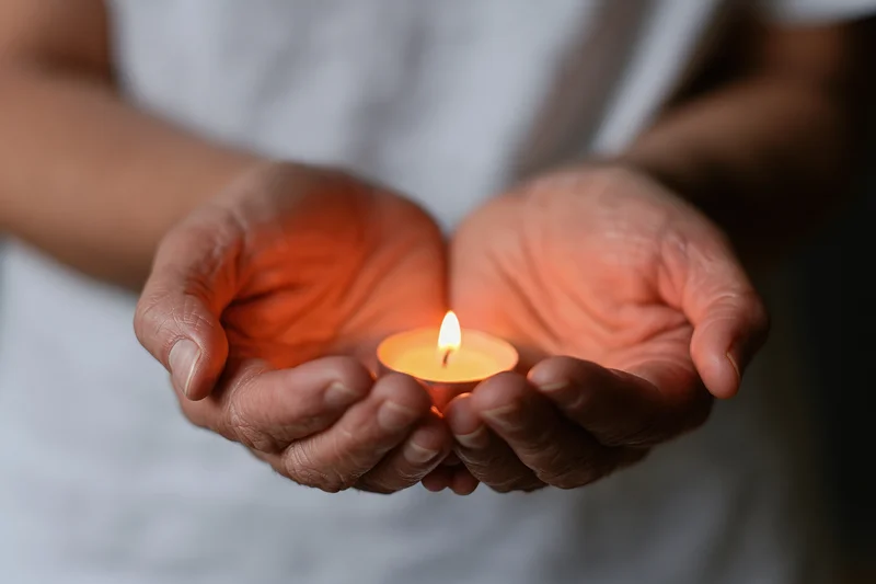 Cupped hands holding a small lit candle in a quiet indoor setting