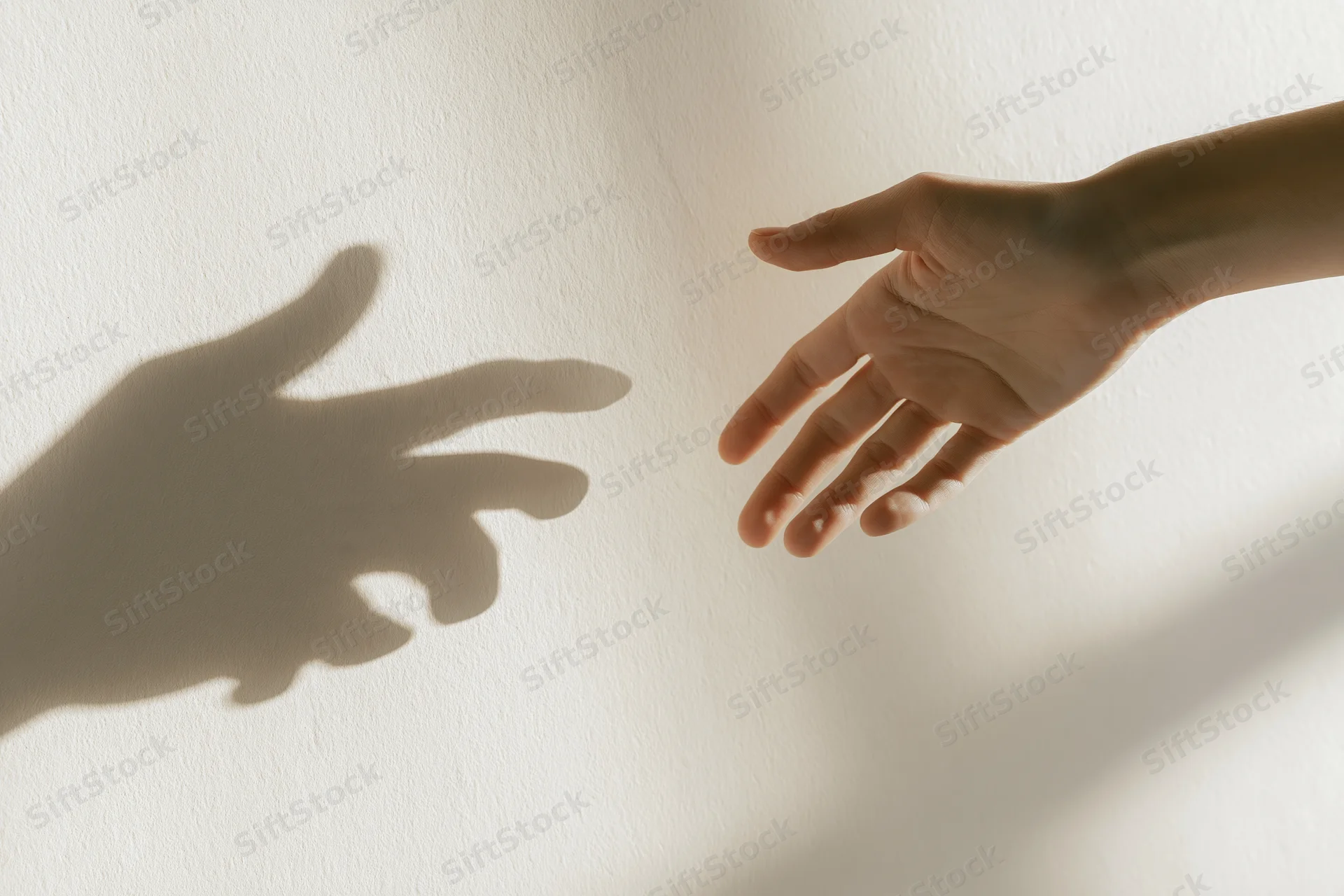 Hand reaching toward its shadow on a white wall