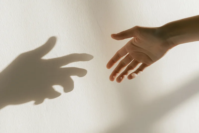 Hand reaching toward its shadow on a white wall