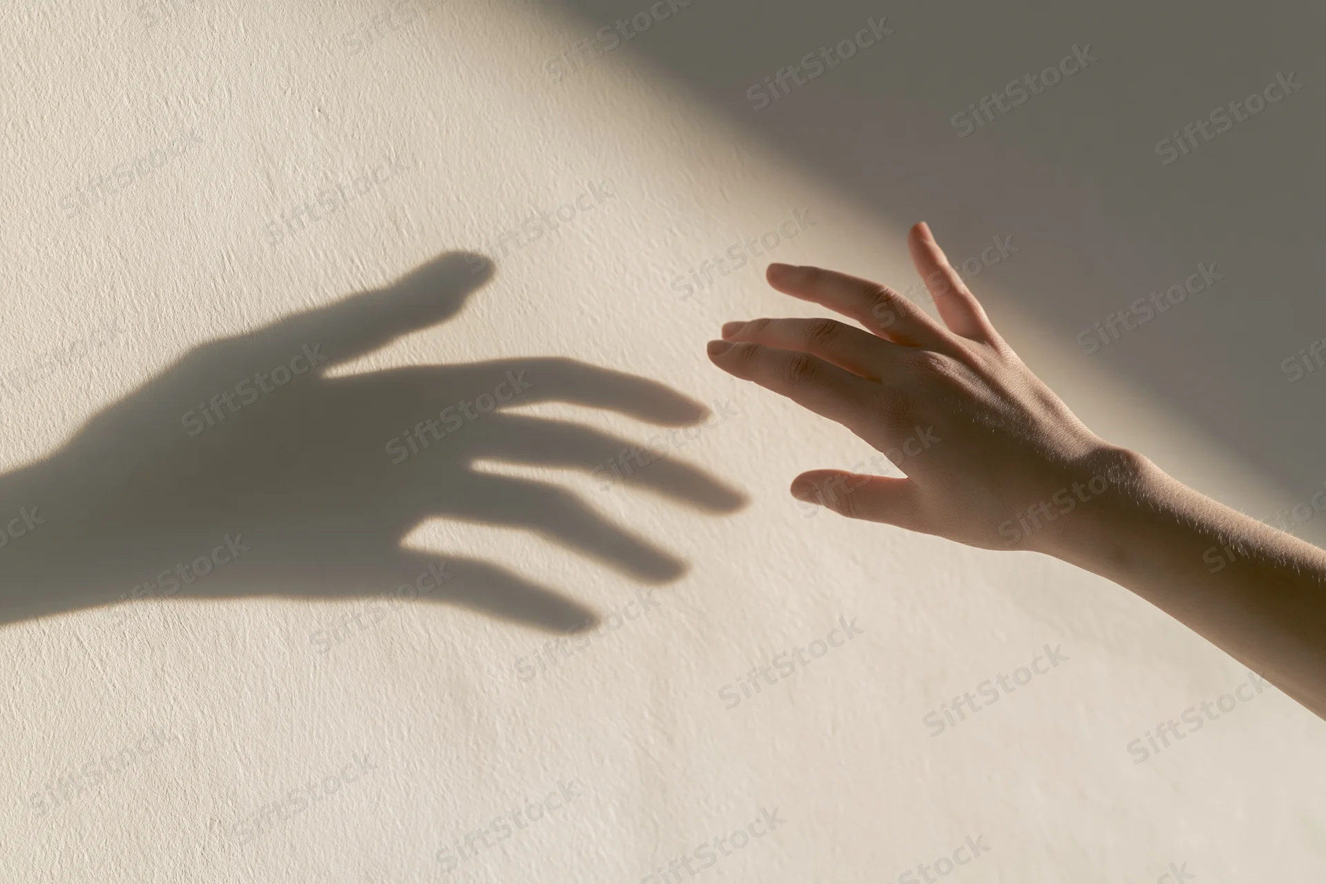 Hand reaching toward its shadow on a sunlit wall