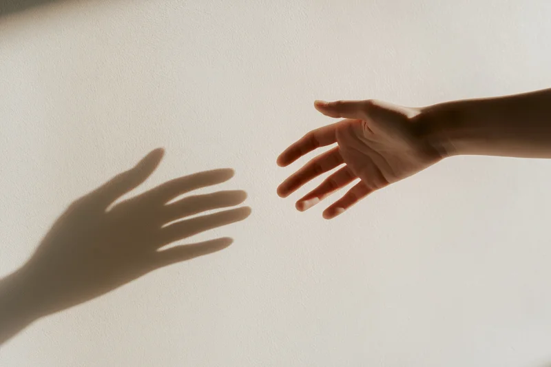Hand reaching toward its shadow on a white wall