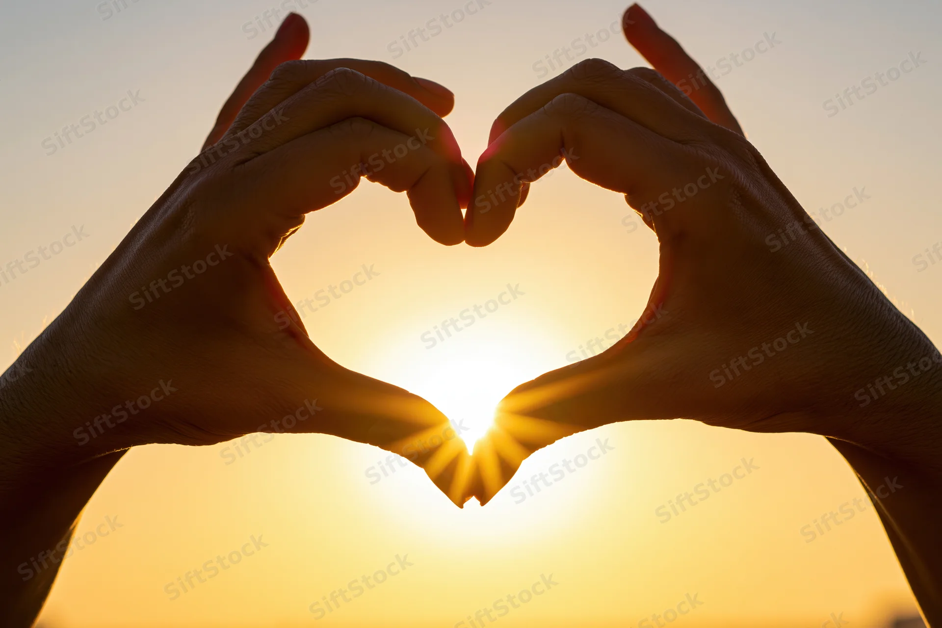 Hands forming heart shape against sunset sky