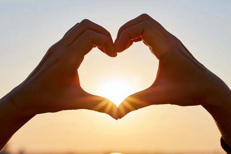 Hands forming a heart shape against a sunset sky