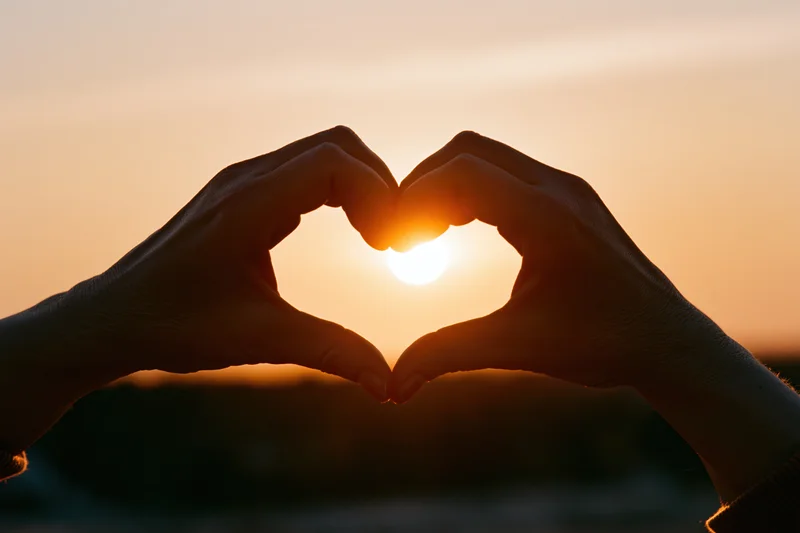 Hands forming a heart shape against a setting sun