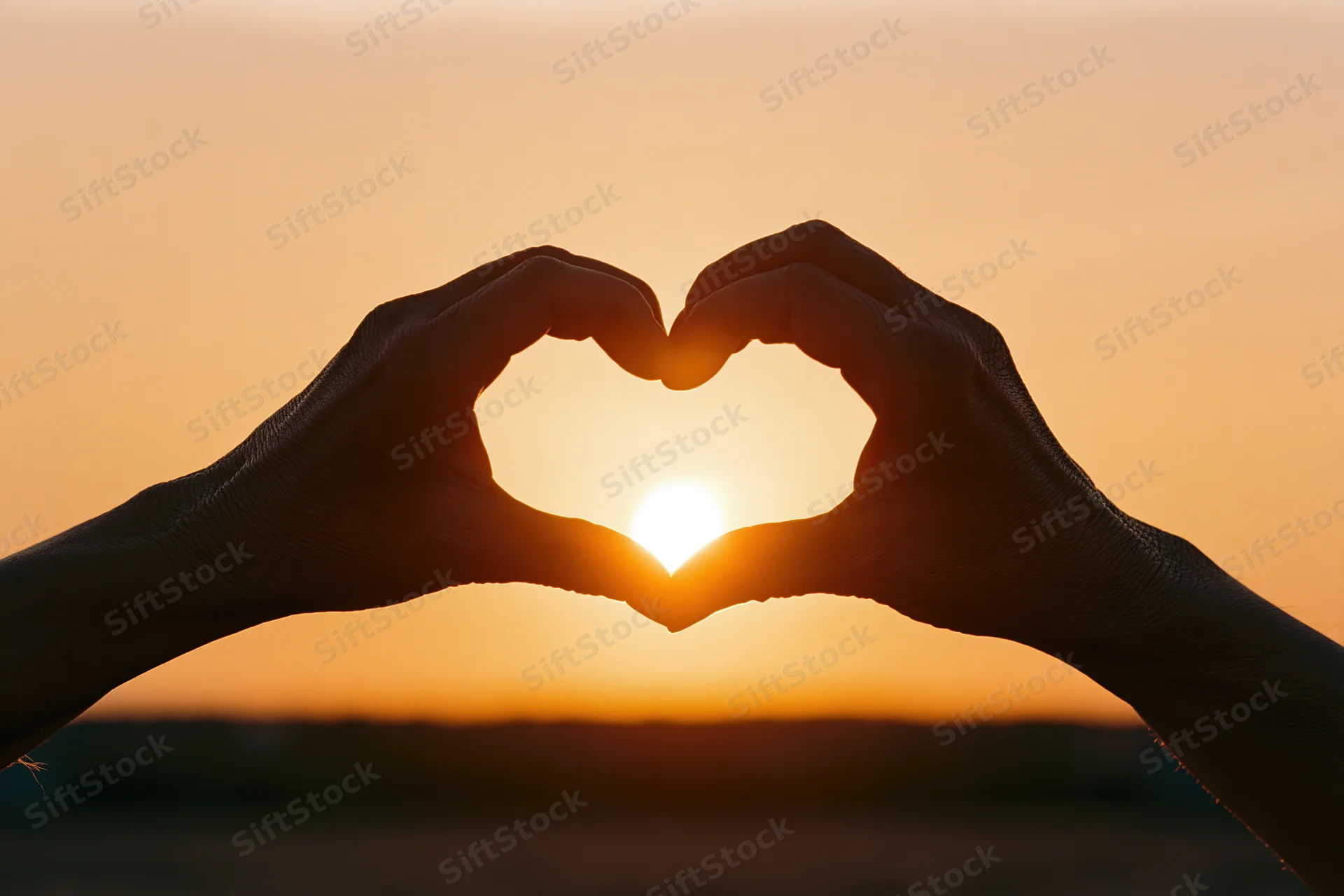 Hands forming a heart shape against a setting sun