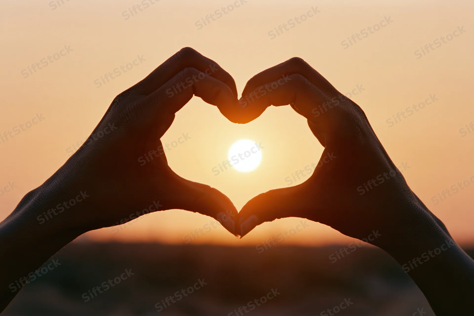 Hands forming heart shape against setting sun