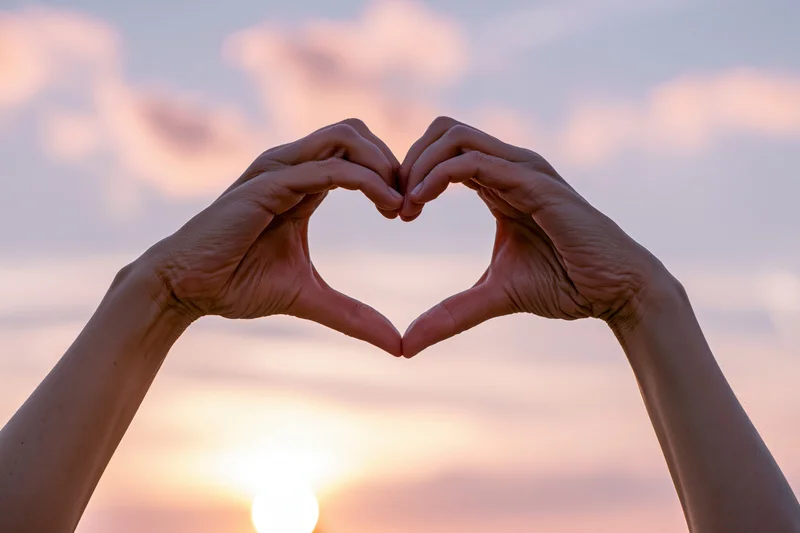 Hands forming a heart shape against a sunset sky
