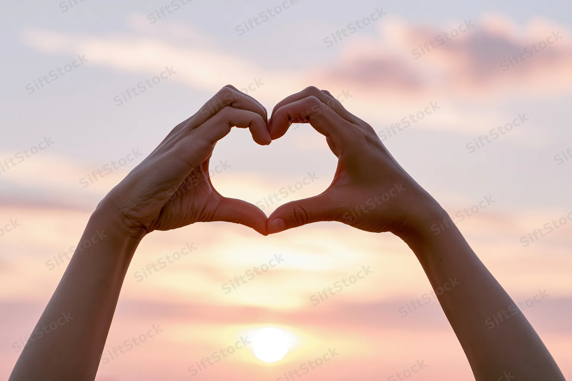 Hands forming a heart shape against a sunset sky