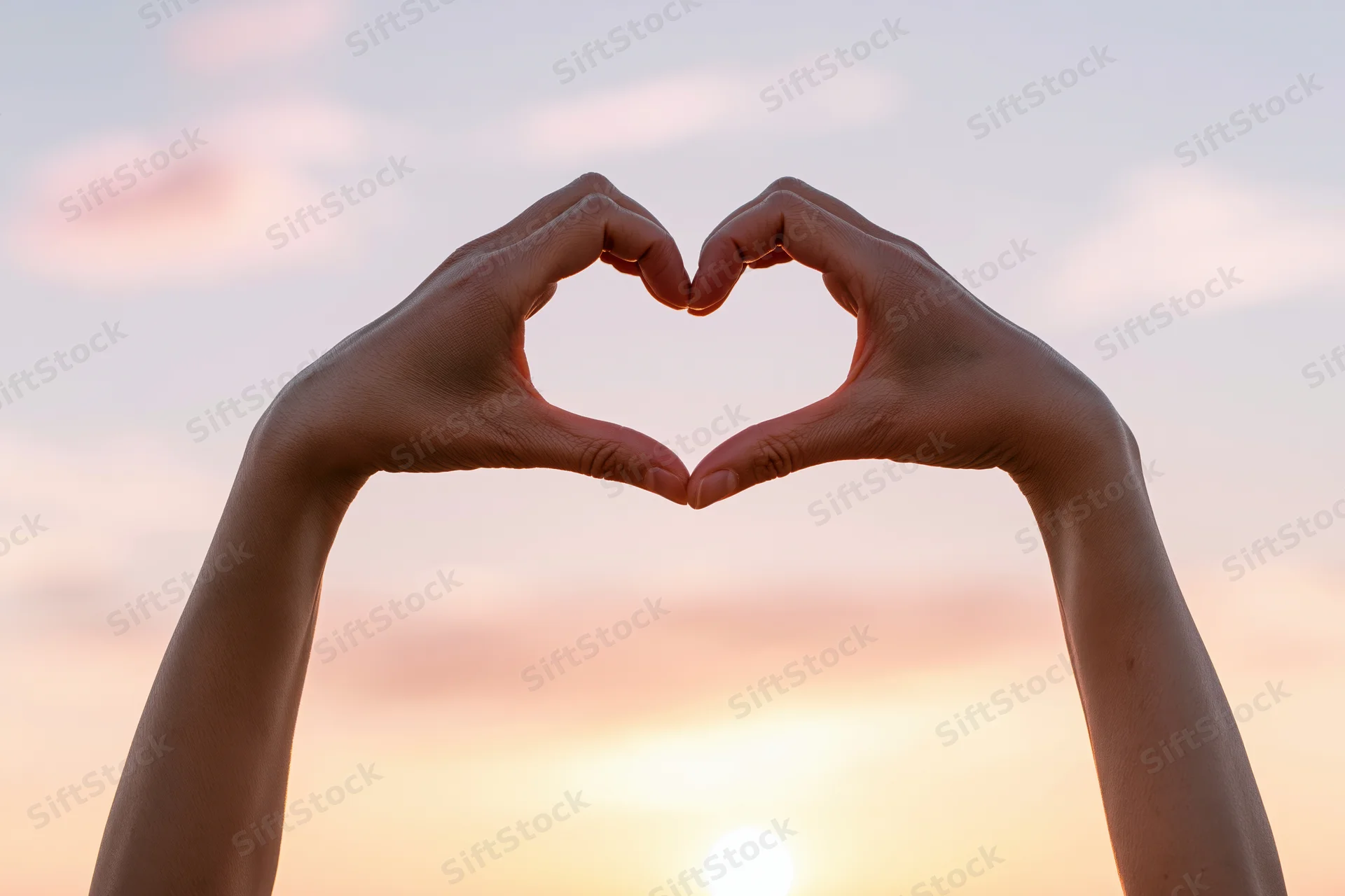 Hands forming a heart shape against a sunset sky