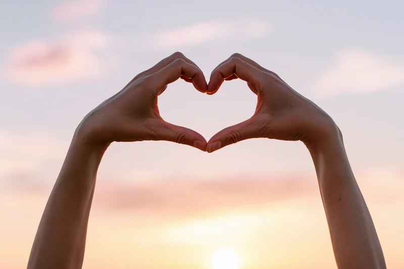 Hands forming a heart shape against a sunset sky