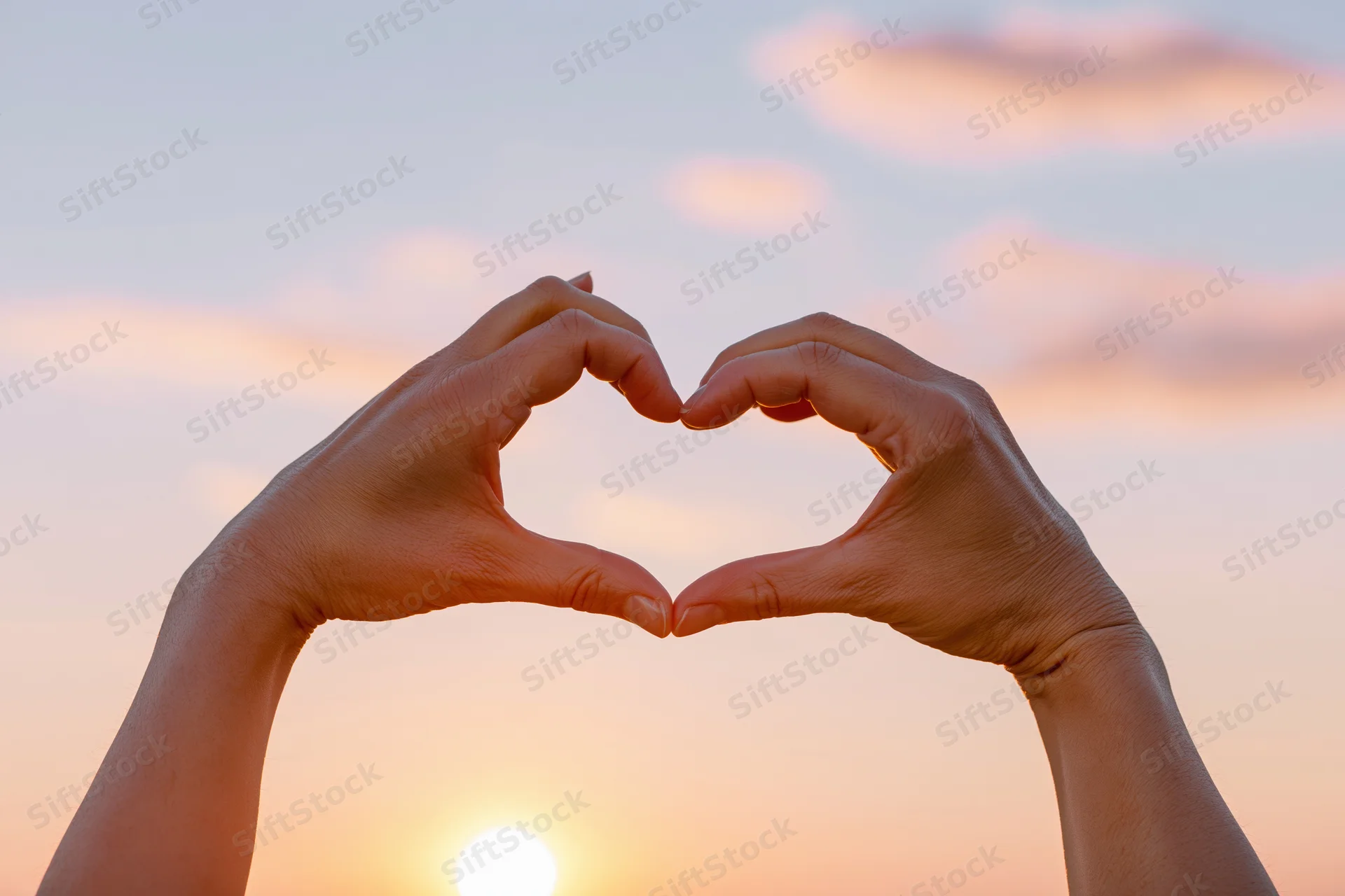 Hands forming a heart shape against a sunset sky