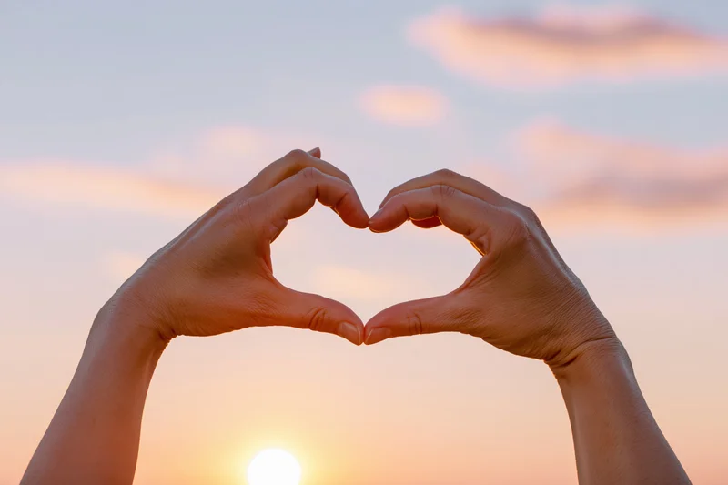 Hands forming a heart shape against a sunset sky