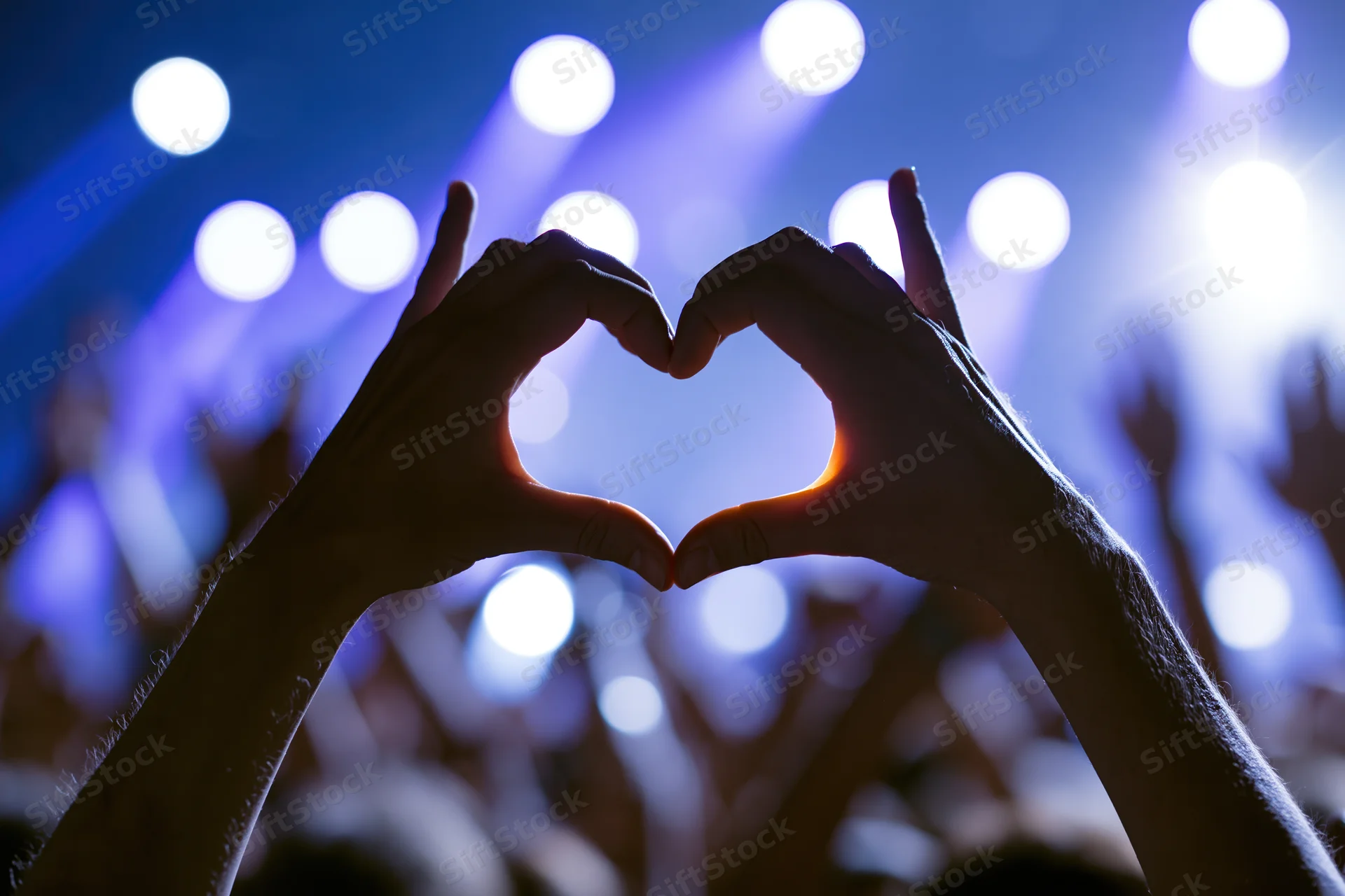 Hands forming heart shape in front of concert stage lights