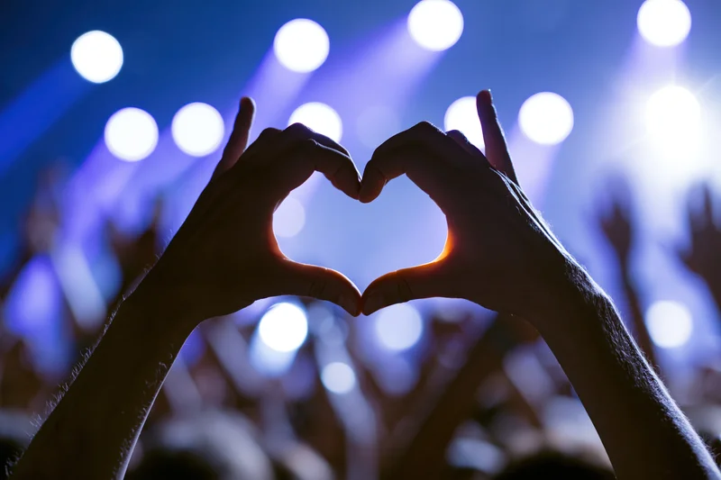 Hands forming heart shape in front of concert stage lights