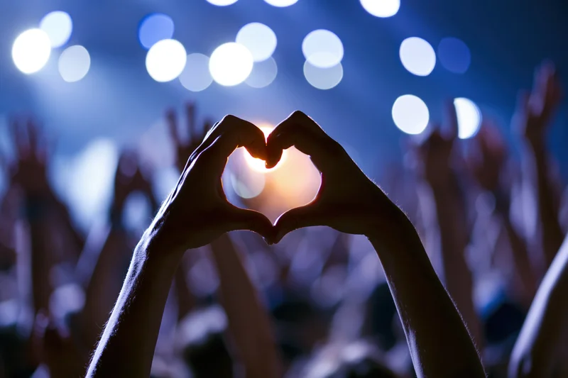 Hands forming heart shape in front of stage lights at concert