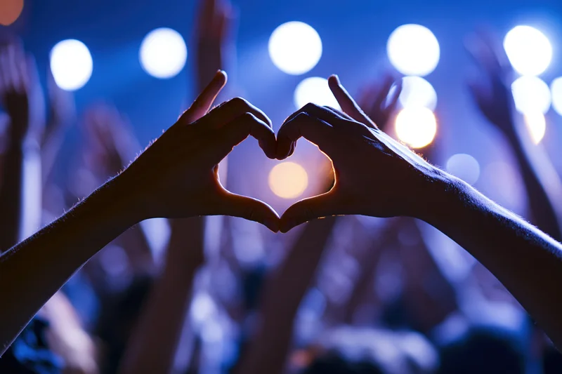 Hands forming heart shape in front of stage lights at concert