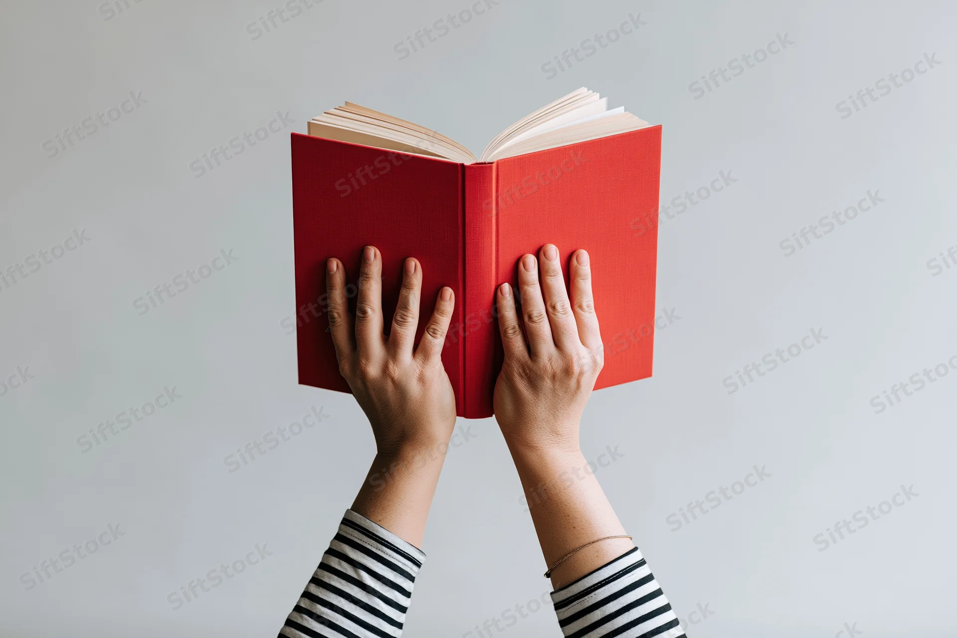 Hands holding open red hardcover book above head against plain background