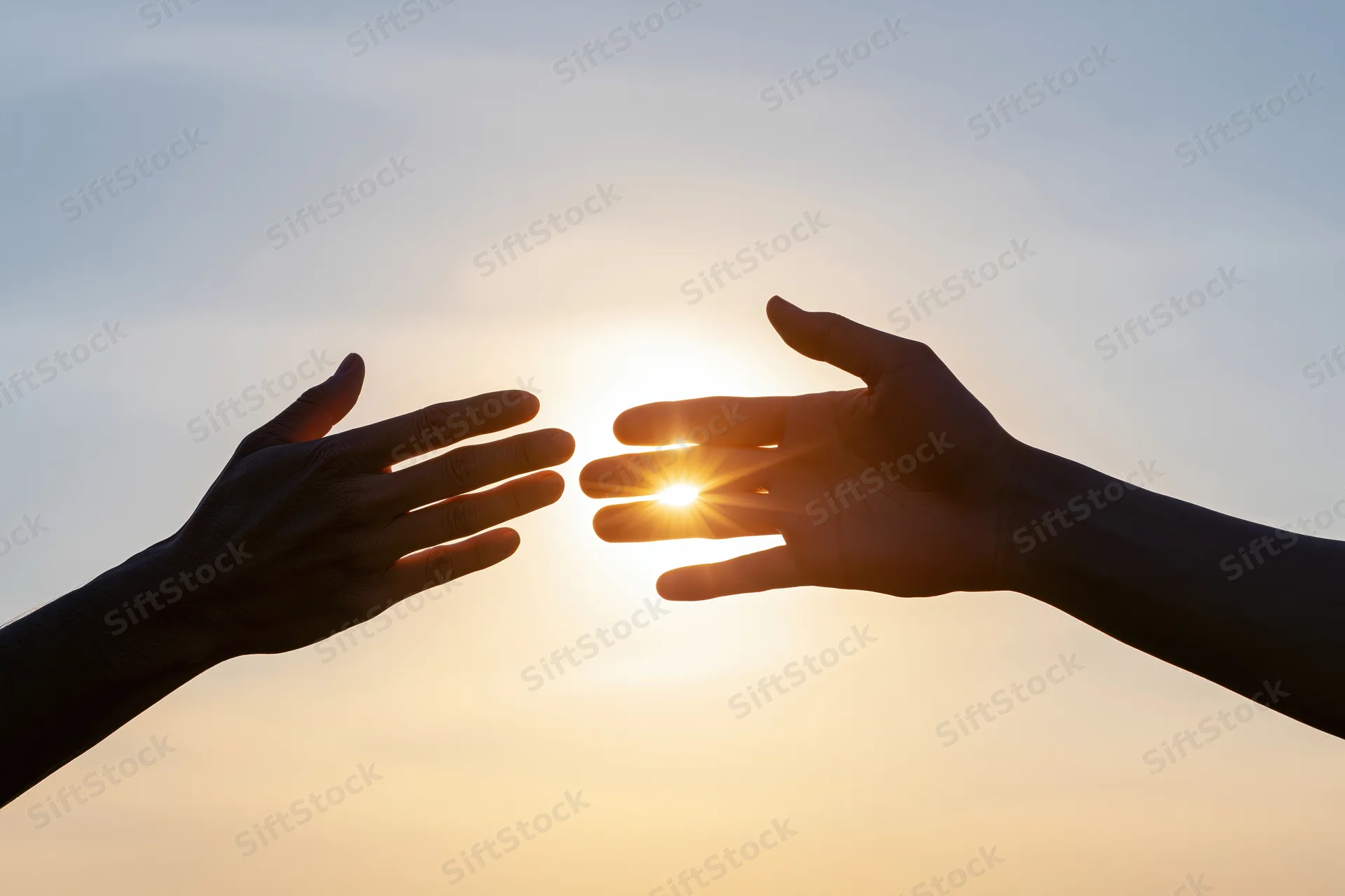 Two hands reaching toward each other against a bright backlit sky at sunrise
