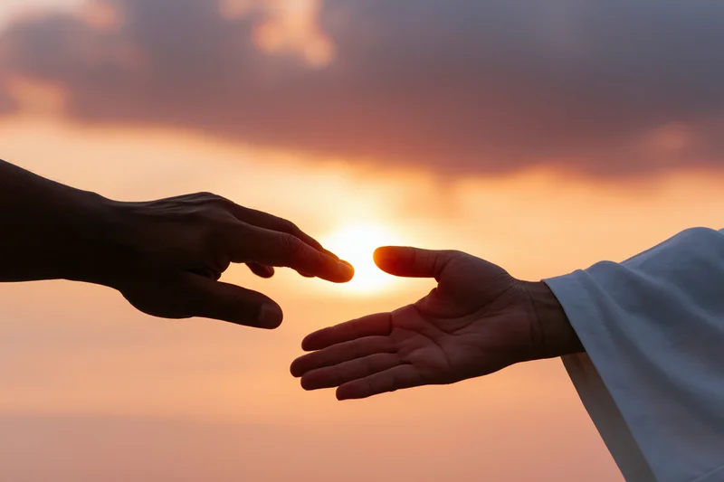 Two hands reaching toward each other against a sunset sky