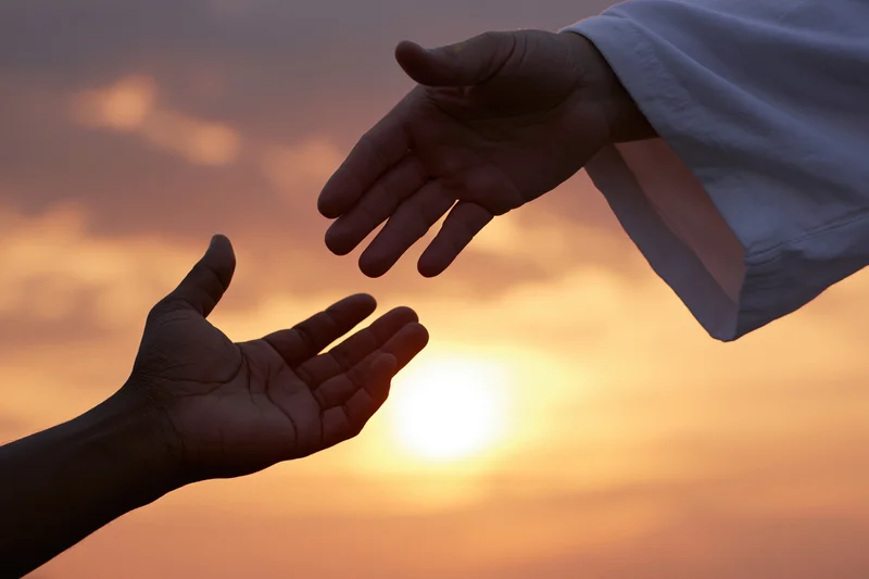 Two hands reaching toward each other in silhouette against a sunset sky