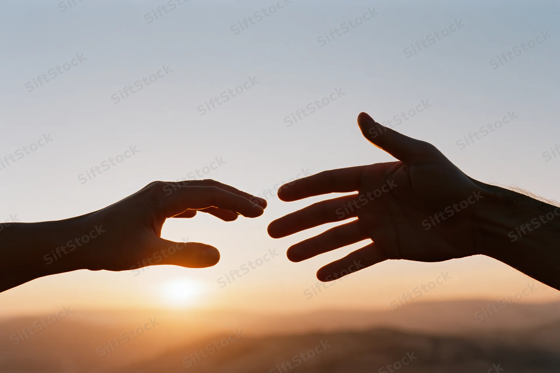 Two hands reaching toward each other in silhouette against a sunset sky