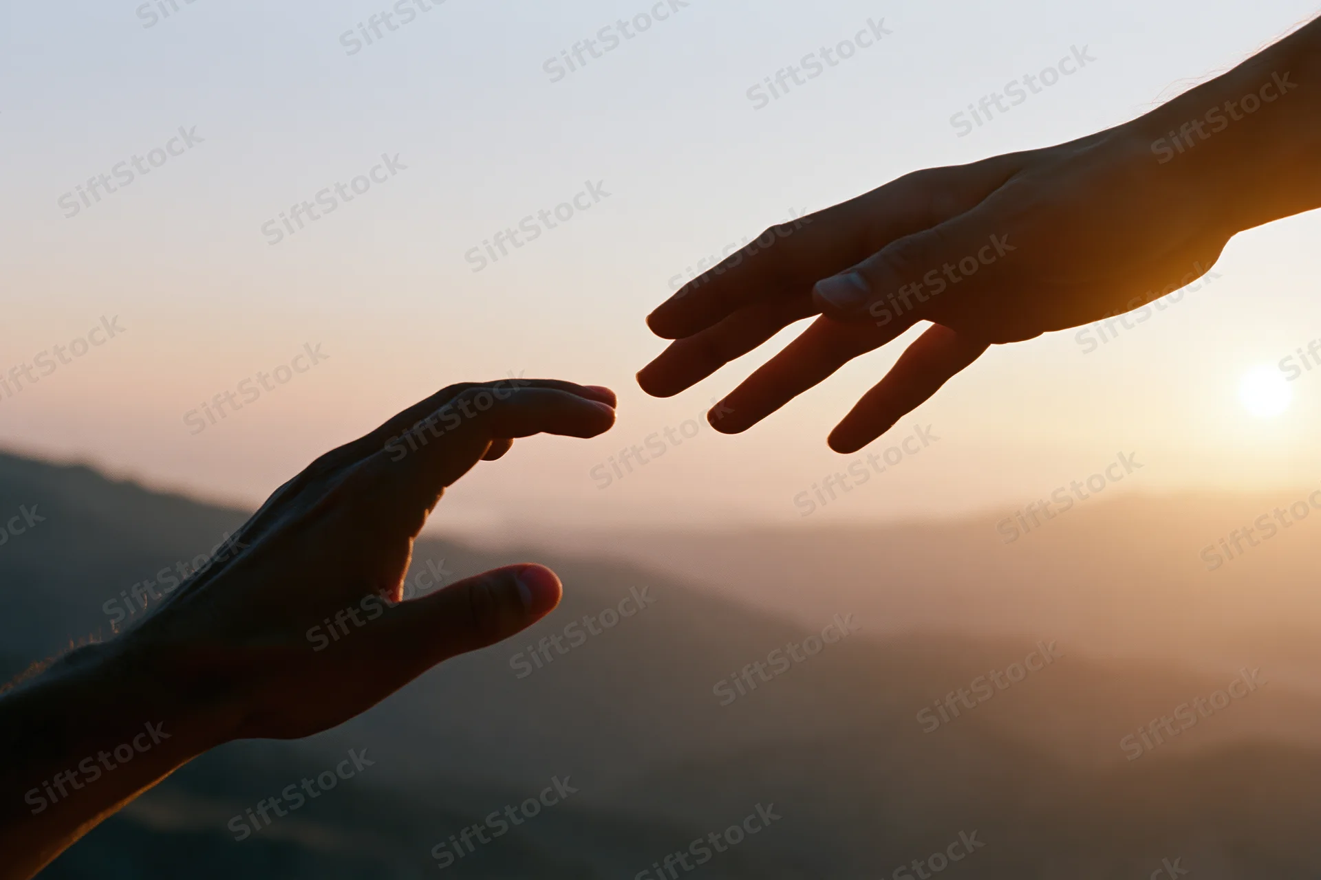 Two hands reaching toward each other in silhouette against a sunset sky