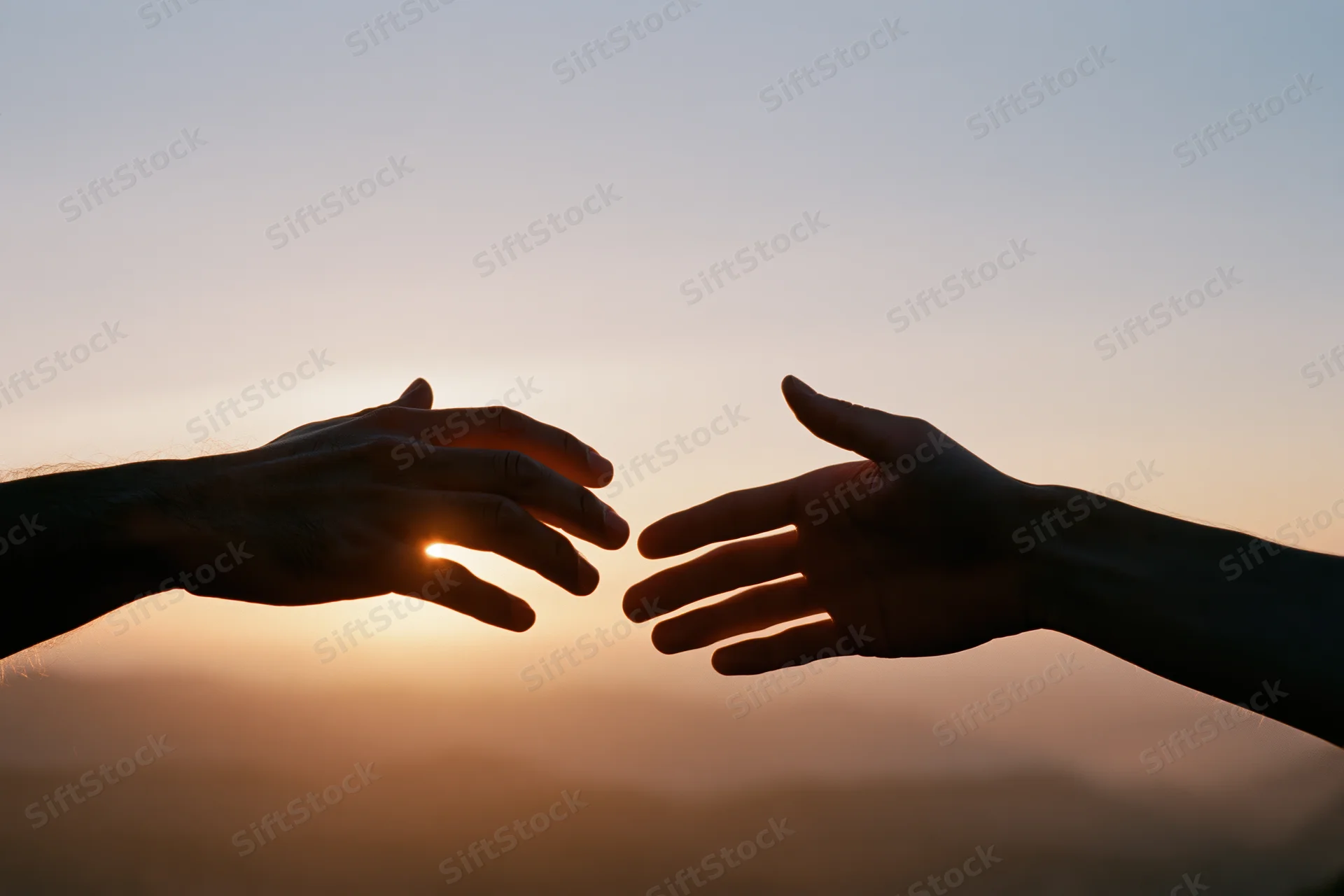 Two hands reaching toward each other in silhouette against a sunset sky