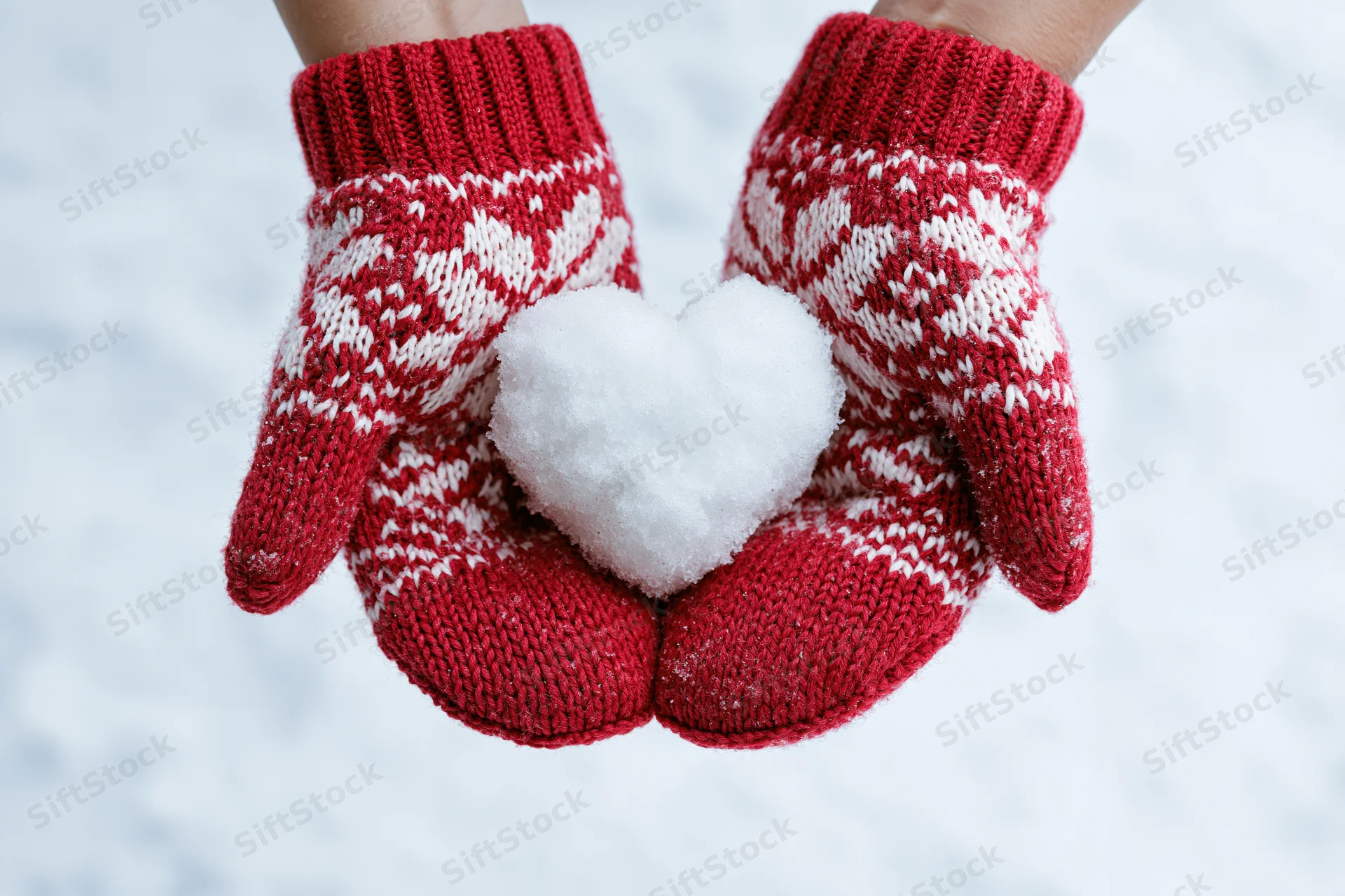 Hands in red knitted mittens holding a snow heart in winter snow