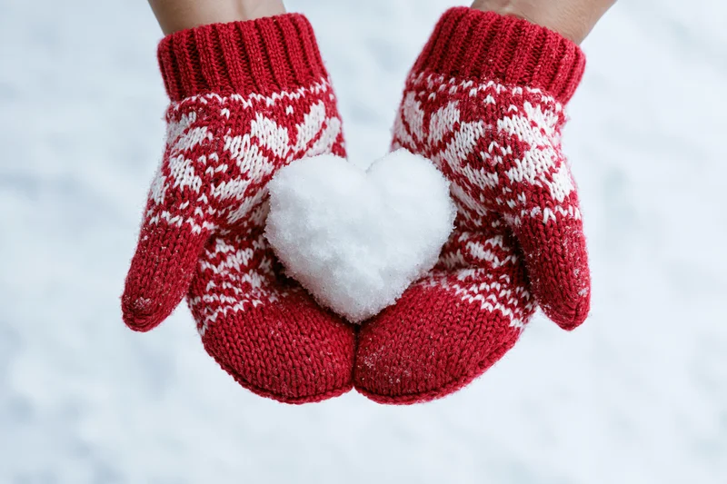 Hands in red knitted mittens holding a snow heart in winter snow