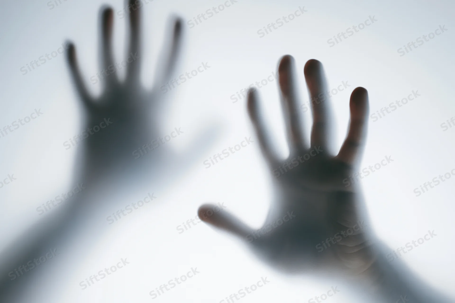 Two hands pressed against frosted glass with fingers spread and palms flat, creating blurred silhouettes against a bright background