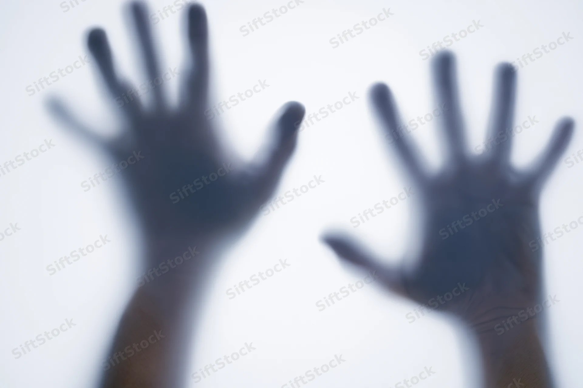Two hands pressed against frosted glass with fingers spread, creating blurred silhouettes against a bright background