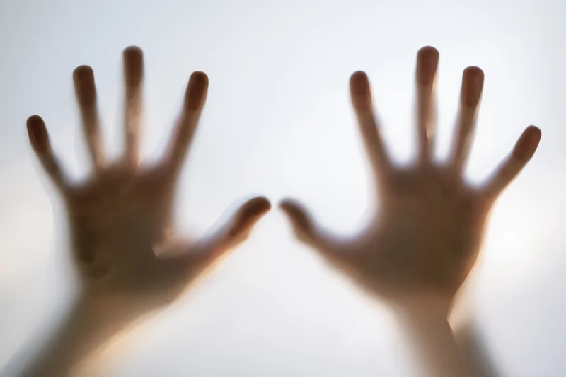 Two human hands pressed flat against frosted glass from behind