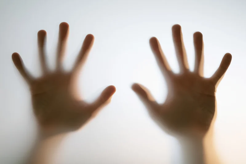 Two human hands pressed flat against frosted glass from behind