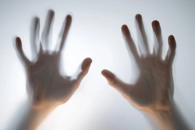 Two human hands pressed flat against frosted glass from behind
