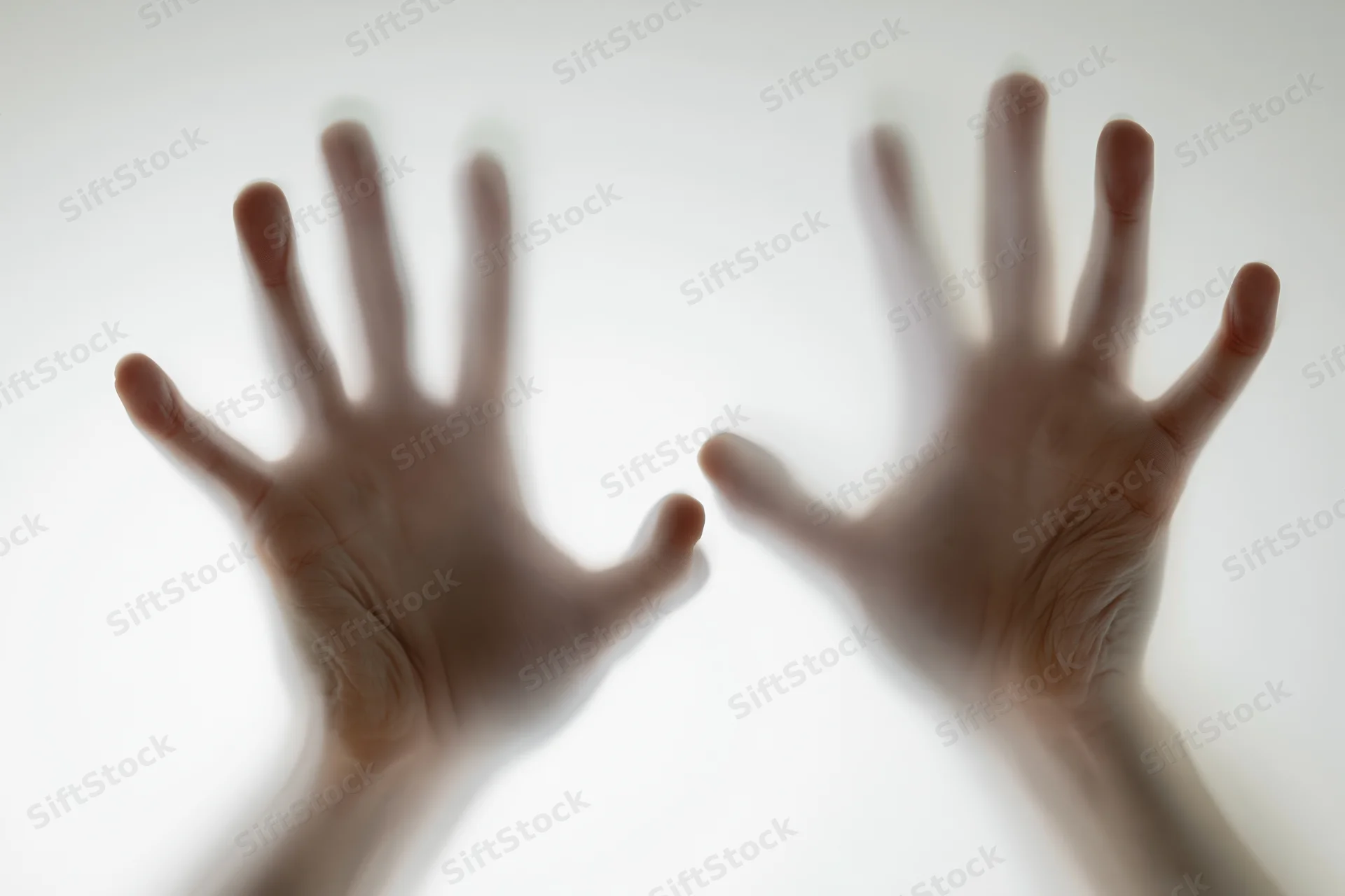 Two hands pressed against frosted glass from behind, fingers spread, palms flat, creating blurred silhouettes against a bright white surface