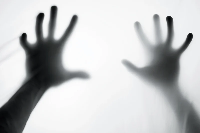 Two hands pressed against frosted glass in a blurred silhouette