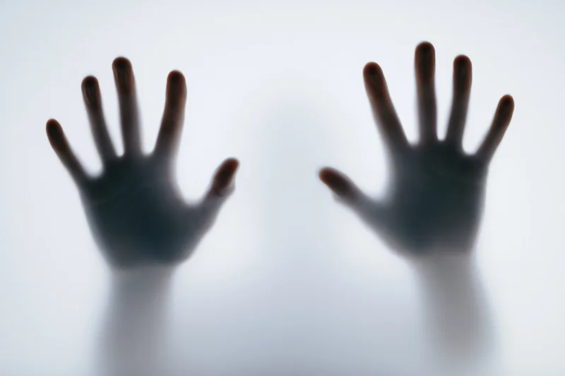 Two human hands pressing against a frosted translucent surface