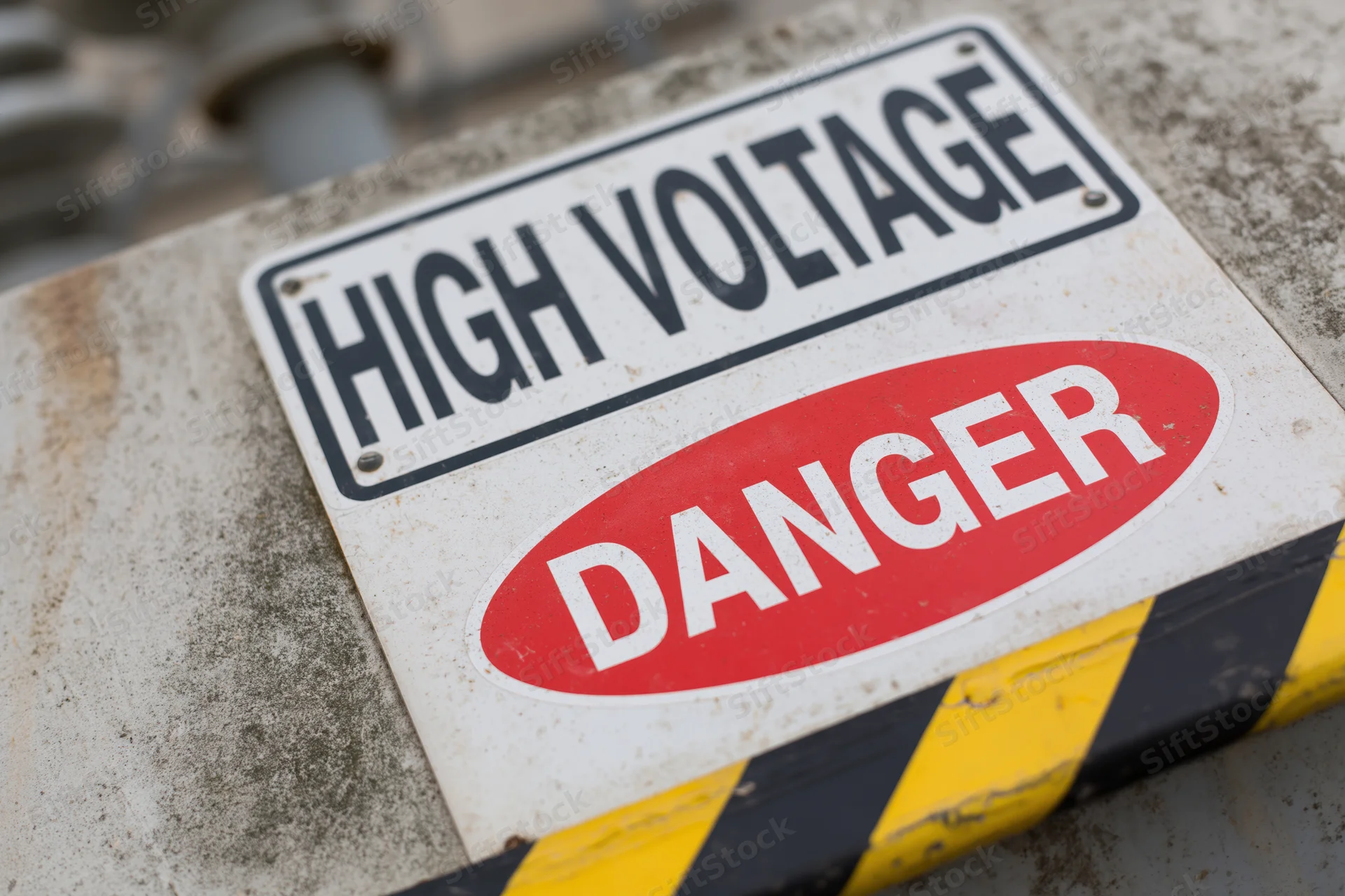 Weathered high voltage danger sign mounted on concrete surface with yellow black stripes