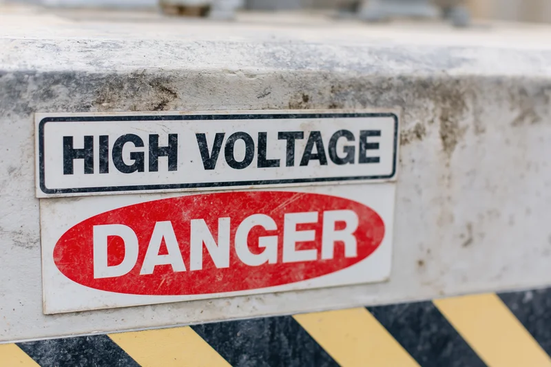 Two warning signs reading high voltage and danger mounted on a weathered concrete surface