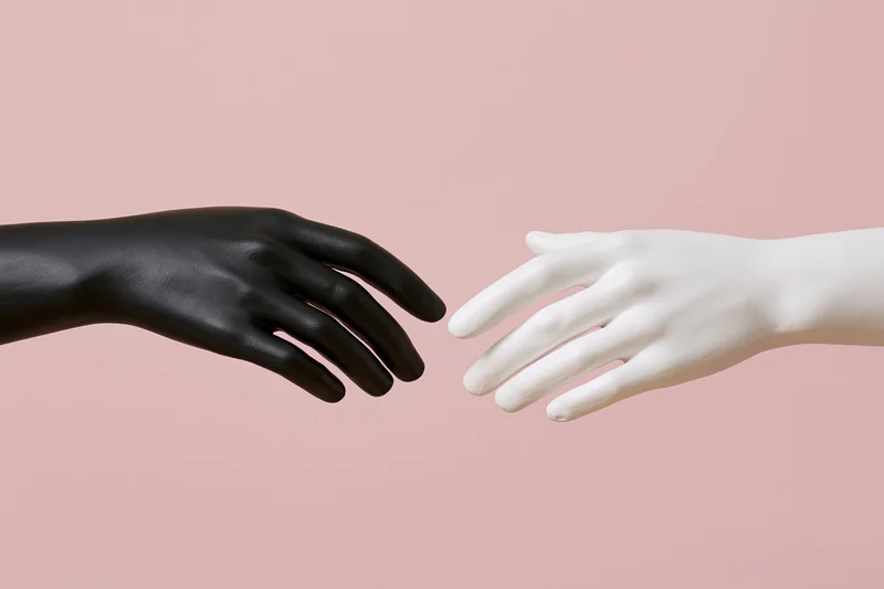 Two mannequin hands reaching toward each other almost touching against a pink background