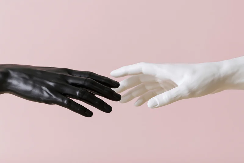 Two mannequin hands reaching toward each other almost touching against a pink background