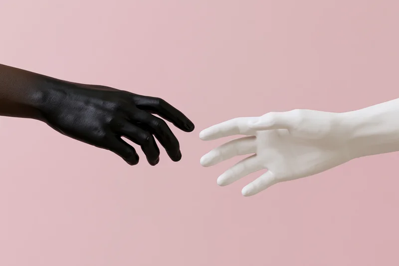 Two mannequin hands reaching toward each other against a pink background