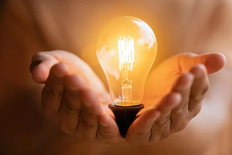 Hands cupping a glowing incandescent light bulb