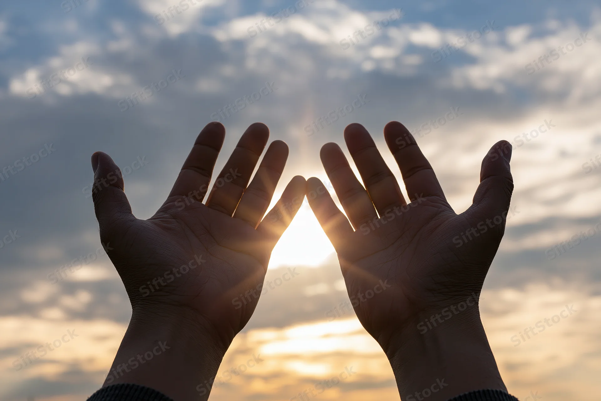 Hands raised palms-up toward the sky at sunrise with sun shining through fingers