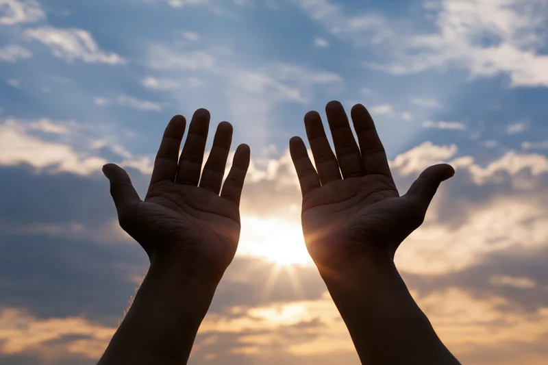 Open hands raised palms-up toward the sky at sunset