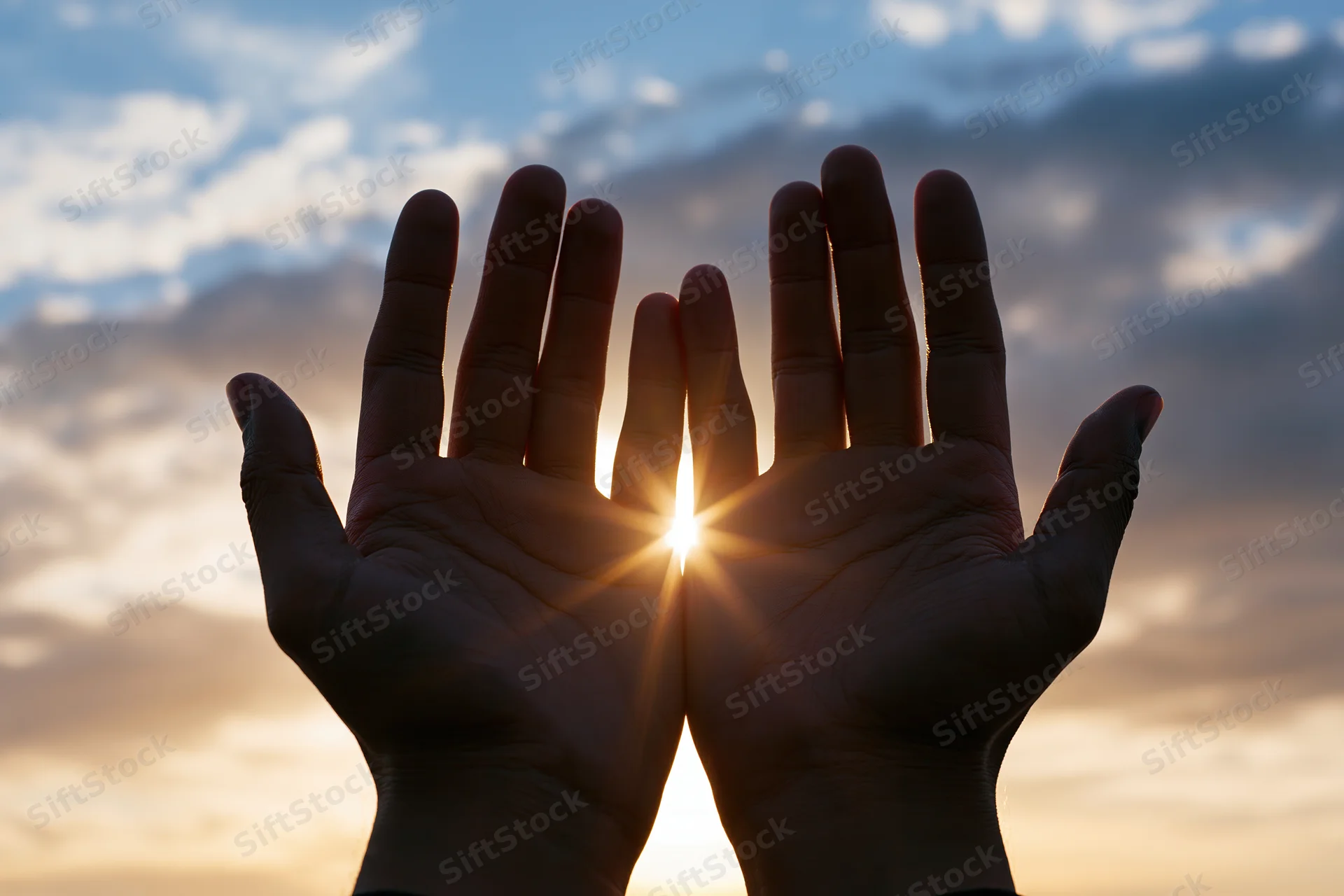 Hands raised palms-up toward the sky with sun shining through at sunrise or sunset