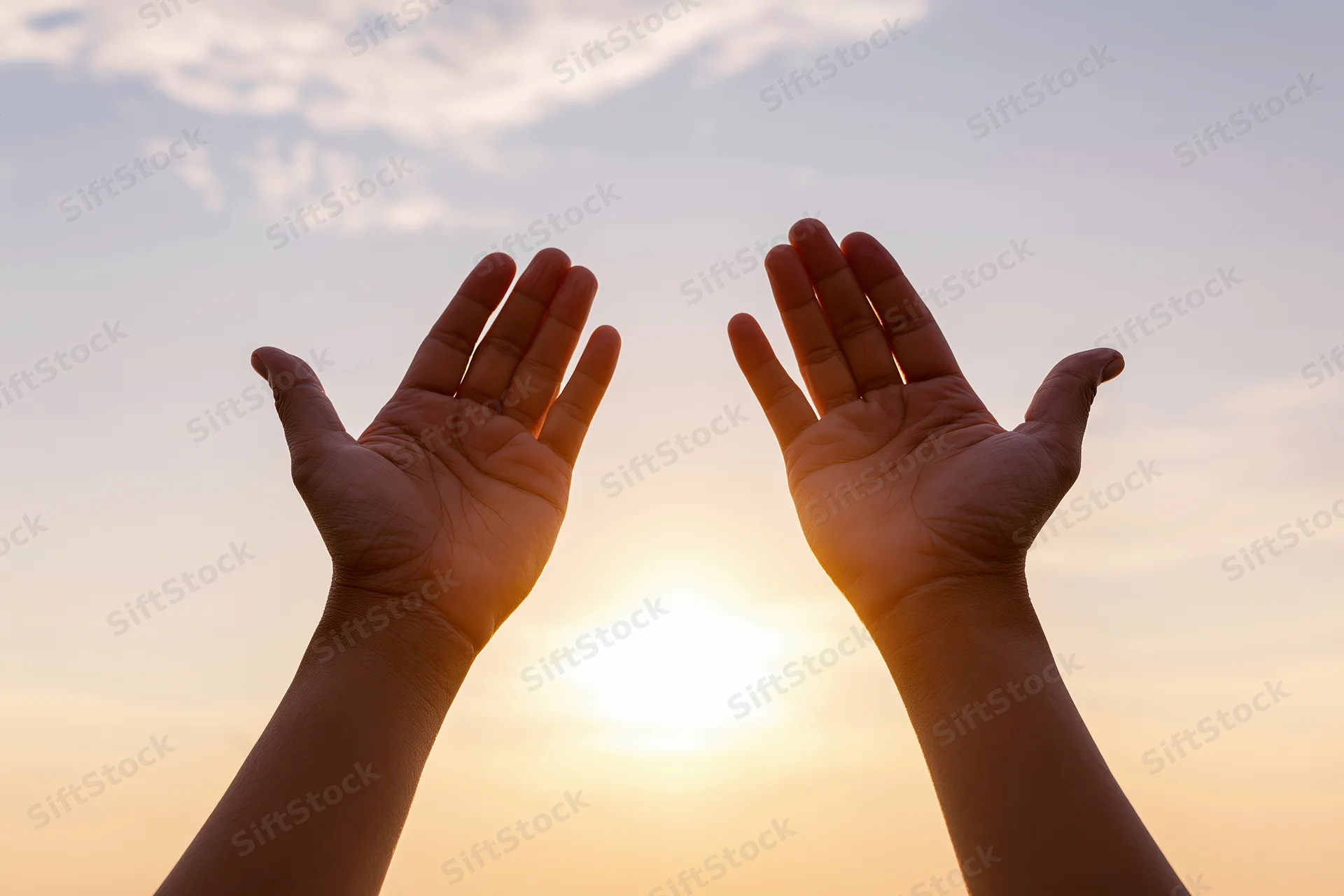 Hands raised upward against a sunset sky with sun between them