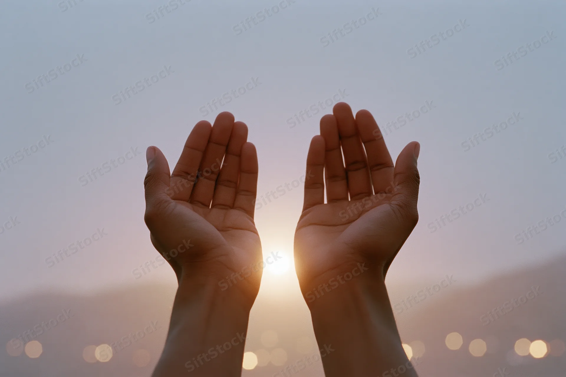 Open hands raised upward in a cupped gesture against a sunrise sky with blurred city lights below