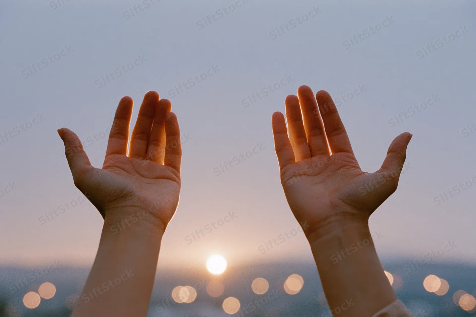 Hands raised in cupped gesture against sunset sky with city lights blurred below