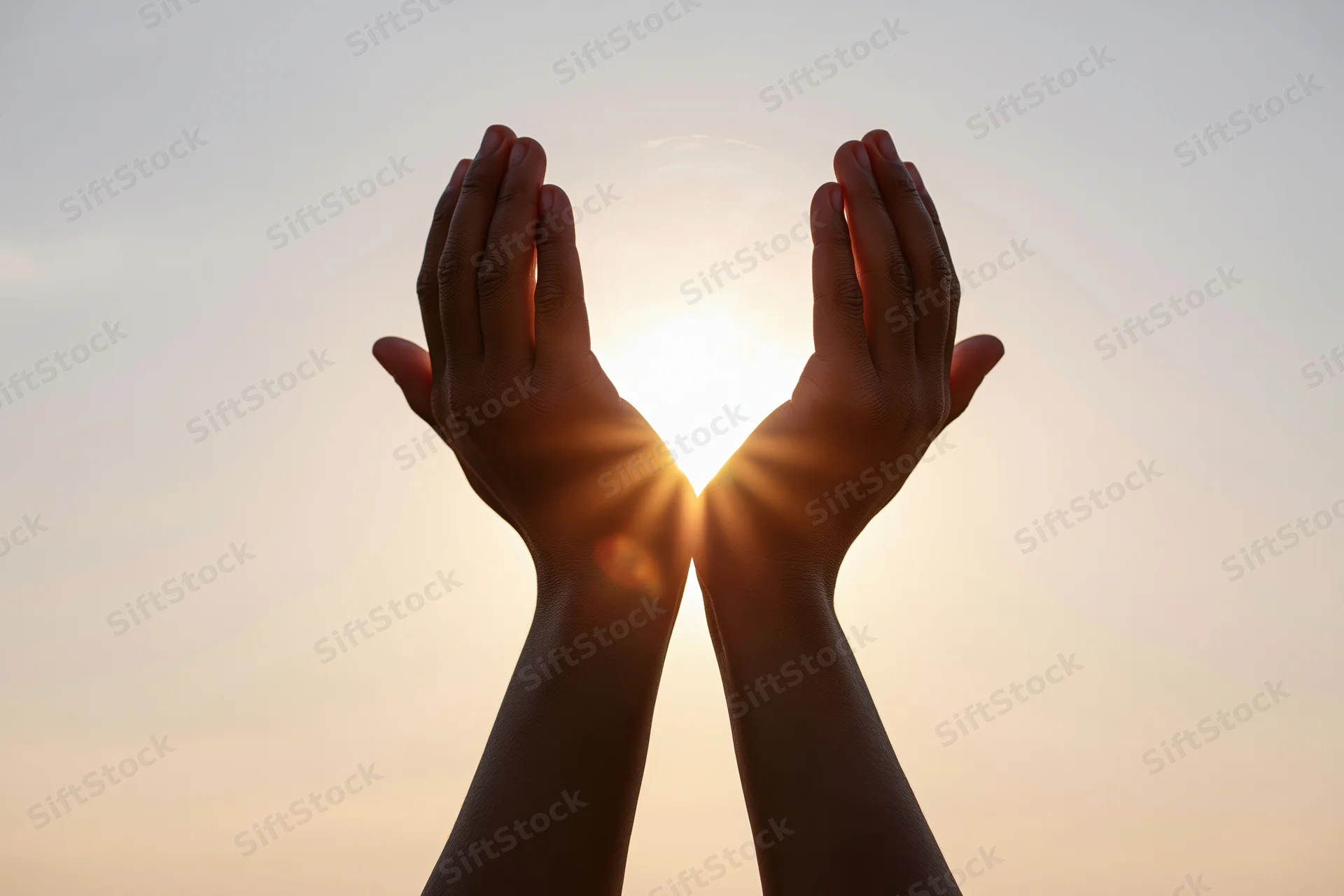 Hands raised upward cupping the sun at sunrise against a clear sky